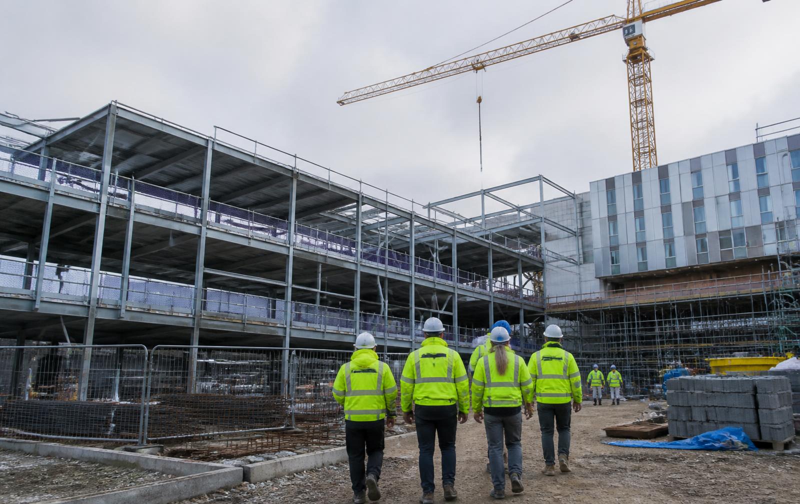 Steel frame of a new hospital wing under construction with a tower crane overhead